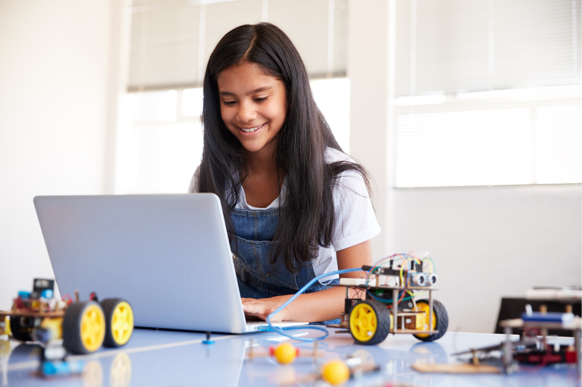 Image of a grade school girl working on a laptop with robots around her
